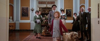 Movie still from “Annie” (1982), directed by John Huston – A group of people standing in a living room; Wide shot, Low angle