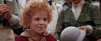 Movie still from “Annie” (1982), directed by John Huston – A little girl with red curly hair is smiling for the camera; Close Up shot, High angle
