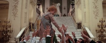 Movie still from “Annie” (1982), directed by John Huston – A group of people reaching up to shake hands on the stairs; Wide shot, High angle