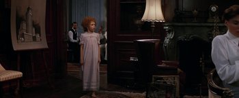 Movie still from “Annie” (1982), directed by John Huston – A little girl standing in front of a living room lamp; Wide shot, Over the shoulder angle