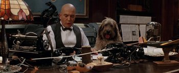 Movie still from “Annie” (1982), directed by John Huston – A man sitting at a table with a dog; Medium shot, Low angle