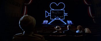 Movie still from “Annie” (1982), directed by John Huston – People sitting in front of an illuminated movie camera; Extreme Wide shot, Over the shoulder angle