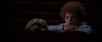 Movie still from “Annie” (1982), directed by John Huston – A little girl and a dog sitting in a movie theater; Medium shot, High angle