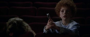 Movie still from “Annie” (1982), directed by John Huston – A woman sitting in a movie theater holding a cell phone; Medium shot, High angle