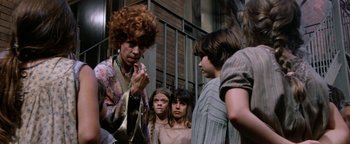 Movie still from “Annie” (1982), directed by John Huston – A group of people standing next to each other on a street; Close Up shot, Over the shoulder angle