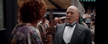 Movie still from “Annie” (1982), directed by John Huston – A man in a suit and bow tie talking to a woman in front of a group of people; Medium shot, Over the shoulder angle
