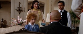 Movie still from “Annie” (1982), directed by John Huston – A group of people in a room with a woman and a child; Medium shot, Over the shoulder angle