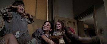 Movie still from “Annie” (1982), directed by John Huston – Two young people sitting on a couch and smiling; Medium shot, Low angle
