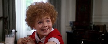 Movie still from “Annie” (1982), directed by John Huston – A young girl with a red shirt and curly red hair smiling; Close Up shot, High angle