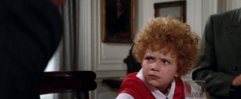 Movie still from “Annie” (1982), directed by John Huston – A young boy sitting at a table in front of a painting; Close Up shot, High angle