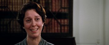 Movie still from “Annie” (1982), directed by John Huston – A woman smiling for the camera in front of a book case; Close Up shot, Low angle