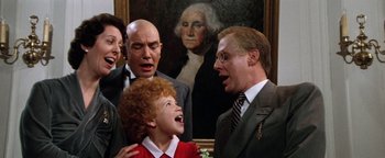 Movie still from “Annie” (1982), directed by John Huston – A group of people standing next to each other in front of a painting; Medium shot, Low angle