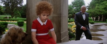 Movie still from “Annie” (1982), directed by John Huston – A little girl in a red dress sitting on the ground; Medium shot, Over the shoulder angle