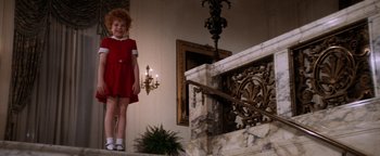 Movie still from “Annie” (1982), directed by John Huston – A little girl in a red dress standing on steps; Wide shot, Low angle