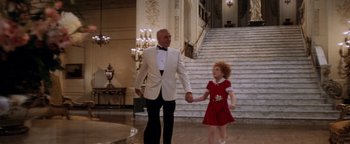 Movie still from “Annie” (1982), directed by John Huston – A man and a little girl holding hands in front of a staircase; Wide shot, Low angle