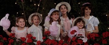 Movie still from “Annie” (1982), directed by John Huston – A group of young girls standing next to each other in front of flowers; Medium shot, High angle