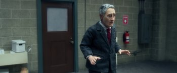 Movie still from “Anomalisa” (2015), directed by Duke Johnson – A man wearing a suit and tie standing in front of a brick wall; Medium shot, Low angle