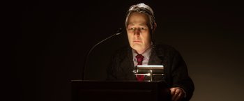 Movie still from “Anomalisa” (2015), directed by Duke Johnson – A man in a suit and tie sitting in front of a microphone; Close Up shot, Low angle