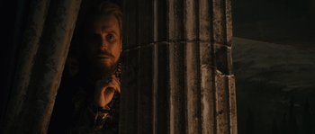 Movie still from “Anonymous” (2011), directed by Roland Emmerich – A man with a beard is standing next to a metal fence; Medium shot, Low angle