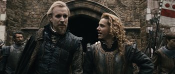 Movie still from “Anonymous” (2011), directed by Roland Emmerich – Two men in medieval garb standing next to each other; Medium shot, Over the shoulder angle