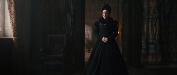 Movie still from “Anonymous” (2011), directed by Roland Emmerich – A woman in a black dress standing next to a fireplace; Medium shot, Over the shoulder angle