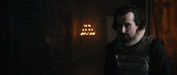 Movie still from “Anonymous” (2011), directed by Roland Emmerich – A man standing in front of a group of lit candles; Medium shot, Over the shoulder angle