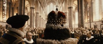 Movie still from “Anonymous” (2011), directed by Roland Emmerich – A crowd of people in an old church with a crown on it; Extreme Wide shot, Low angle