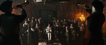 Movie still from “Anonymous” (2011), directed by Roland Emmerich – A group of people standing in a room with a man sitting in a chair; Wide shot, High angle