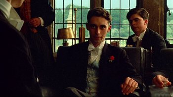 Movie still from “Another Country” (1984), directed by Marek Kanievska – A man sitting in a chair wearing a suit and tie; Medium shot, Low angle