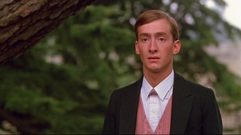 Movie still from “Another Country” (1984), directed by Marek Kanievska – A man in a suit and tie standing in front of a tree; Close Up shot, Low angle