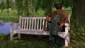 Movie still from “Another Country” (1984), directed by Marek Kanievska – A man sitting on top of a white wooden bench; Medium shot, Low angle
