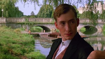 Movie still from “Another Country” (1984), directed by Marek Kanievska – A man in a suit and tie standing in front of a river; Close Up shot, Low angle