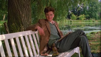 Movie still from “Another Country” (1984), directed by Marek Kanievska – A man sitting on top of a white wooden bench; Medium shot, Low angle