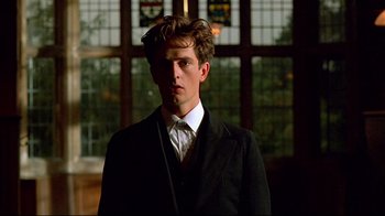 Movie still from “Another Country” (1984), directed by Marek Kanievska – A man in a suit and tie standing in front of stained glass windows; Close Up shot, Low angle