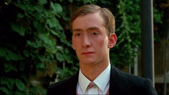Movie still from “Another Country” (1984), directed by Marek Kanievska – A man in a suit and tie standing in front of trees; Close Up shot, Low angle