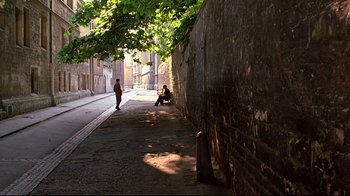 Movie still from “Another Country” (1984), directed by Marek Kanievska – Two people are sitting on a bench on the side of the street; Wide shot, High angle