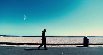 Movie still from “Another Earth” (2011), directed by Mike Cahill – A man is walking on the sidewalk near the ocean; Wide shot, Low angle