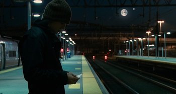 Movie still from “Another Earth” (2011), directed by Mike Cahill – A man standing on a train platform looking at his cell phone; Wide shot, Low angle