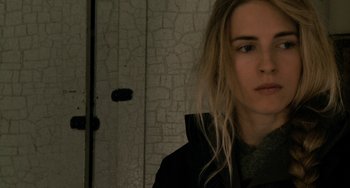 Movie still from “Another Earth” (2011), directed by Mike Cahill – A woman with long blonde hair standing in front of a wall; Close Up shot, Over the shoulder angle