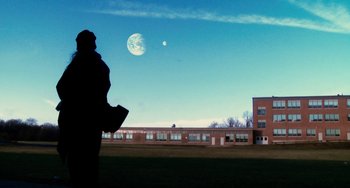 Movie still from “Another Earth” (2011), directed by Mike Cahill – A person standing in front of a building with a moon in the background; Extreme Wide shot, Low angle