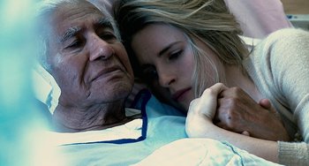 An old man and a young woman laying in bed