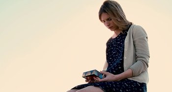 Movie still from “Another Earth” (2011), directed by Mike Cahill – A woman sitting on the ground looking at her cell phone; Medium shot, Low angle
