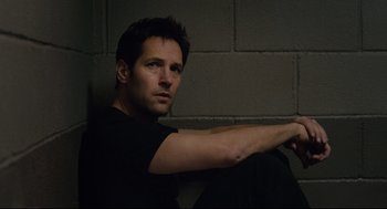 Movie still from “Ant-Man” (2015), directed by Peyton Reed – A man sitting on the ground in front of a brick wall; Medium shot, High angle
