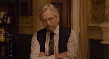 Movie still from “Ant-Man” (2015), directed by Peyton Reed – An older man with a beard and glasses is posing for a picture; Medium shot, Over the shoulder angle