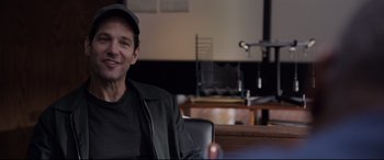 Movie still from “Ant-Man and the Wasp” (2018), directed by Peyton Reed – A man sitting at a table in front of a microphone; Medium shot, Over the shoulder angle