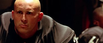 Movie still from “Any Given Sunday” (1999), directed by Oliver Stone – A bald man wearing a leather jacket and ear buds; Close Up shot, Low angle