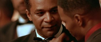 Movie still from “Any Given Sunday” (1999), directed by Oliver Stone – A person wearing a suit and a bow tie; Close Up shot, Over the shoulder angle