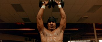 Movie still from “Any Given Sunday” (1999), directed by Oliver Stone – A man is lifting some weights in a gym; Close Up shot, Low angle