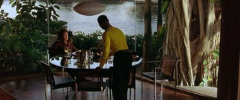 Movie still from “Any Given Sunday” (1999), directed by Oliver Stone – A man standing at a table in front of water; Wide shot, Over the shoulder angle