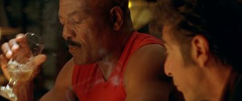 Movie still from “Any Given Sunday” (1999), directed by Oliver Stone – A man in a red shirt is smoking a cigarette; Close Up shot, Low angle